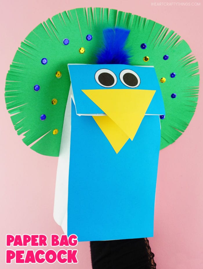 Vertical close up image of adult with hand inside the peacock puppet, making the beak open. Words "Paper Bag Peacock" in bottom left corner.