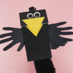 Adult with their hand inside the paper bag crow puppet showing how to make the beak open and close.