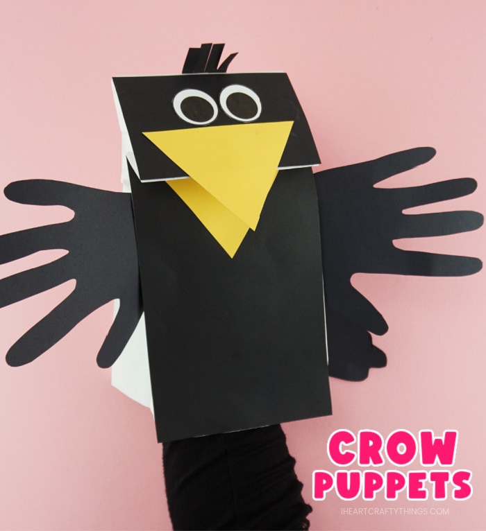 Close up image of adult with their hand in the paper bag puppet showing how to make the crow beak open and close. The words "Crow Puppets" are in the bottom right corner.