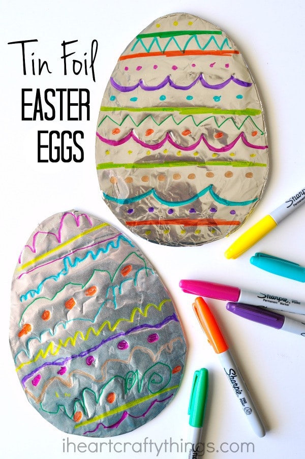 Vertical image of two decorated tin foil Easter Egg art projects laying one on top of the other with Sharpie markers scattered around them and the words "Tin Foil Easter Eggs" in the top left corner.