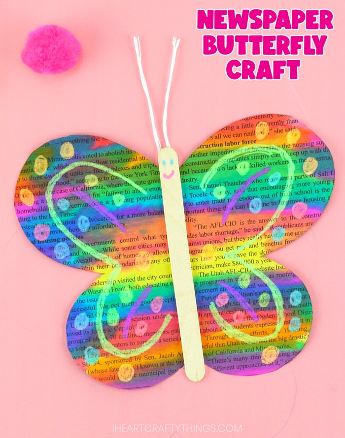 Close up vertical image of butterfly craft laying on a pink background with the words "newspaper butterfly craft" in the top right corner.