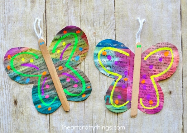 two painted newspaper butterfly crafts laying on a faux wood background