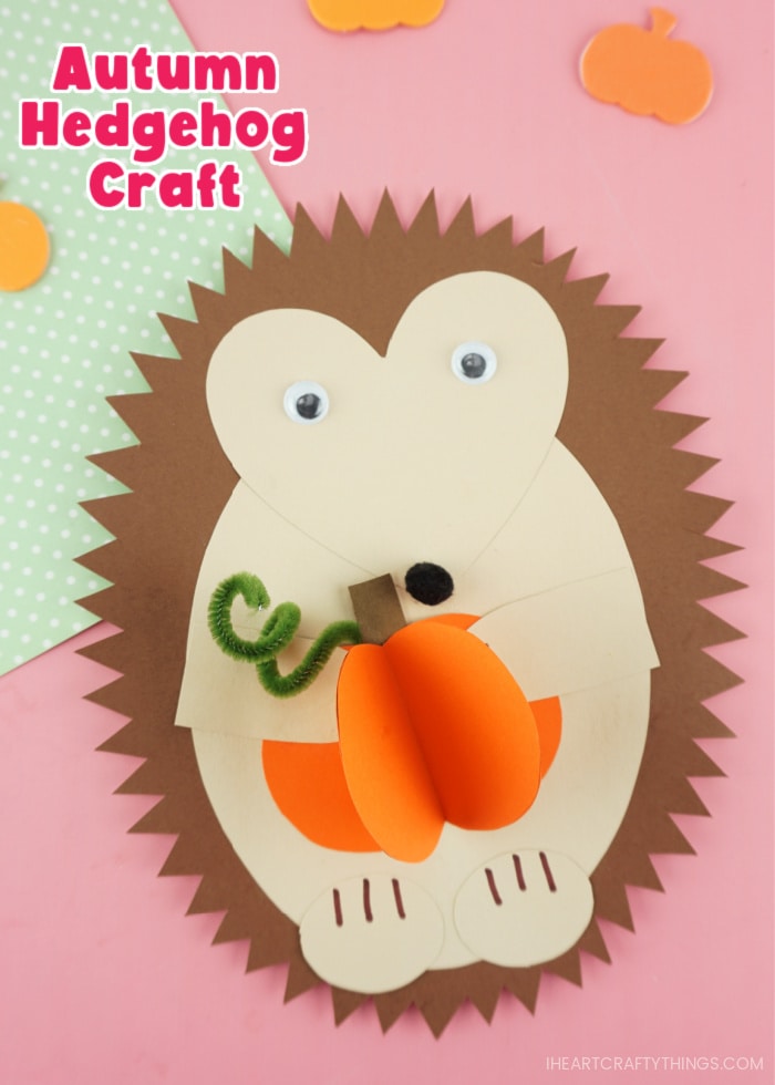 Vertical close up image of paper hedgehog craft holding a 3D paper pumpkin with the words "Autumn Hedgehog Craft" in the top left corner.