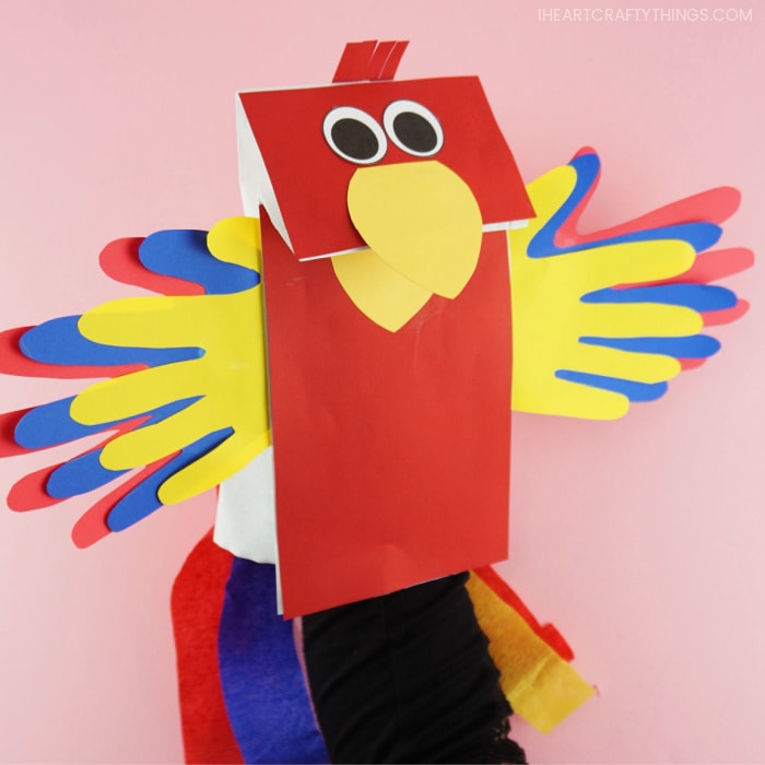 Close up side angle view of paper bag parrot puppet with a hand inside it opening the parrot beak.