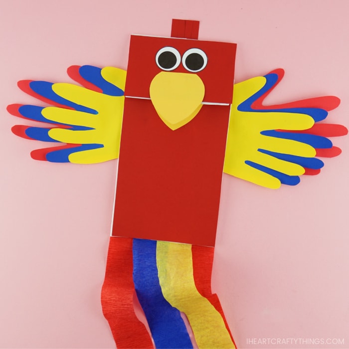 Completed paper bag parrot craft laying flat on a pink background.