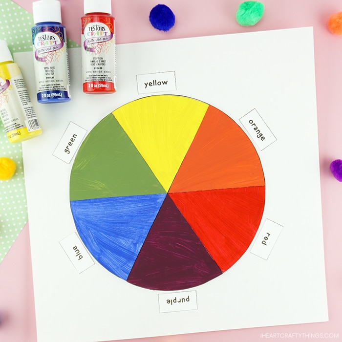 Square close up image of color mixing craft laying on a pink background with bottles of Testors yellow, blue and red paint bottles laying in the top left corner.