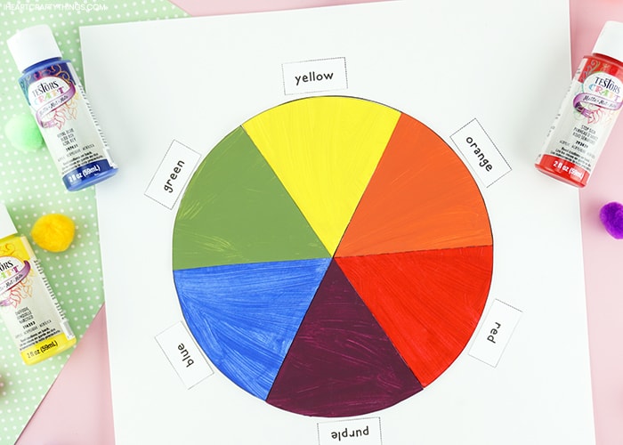 Horizontal close up image of finished color wheel craft with Testors red, blue and yellow paint bottles laying around it.