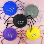 Five paper plates spiders in different colors clumped together on a pink background.