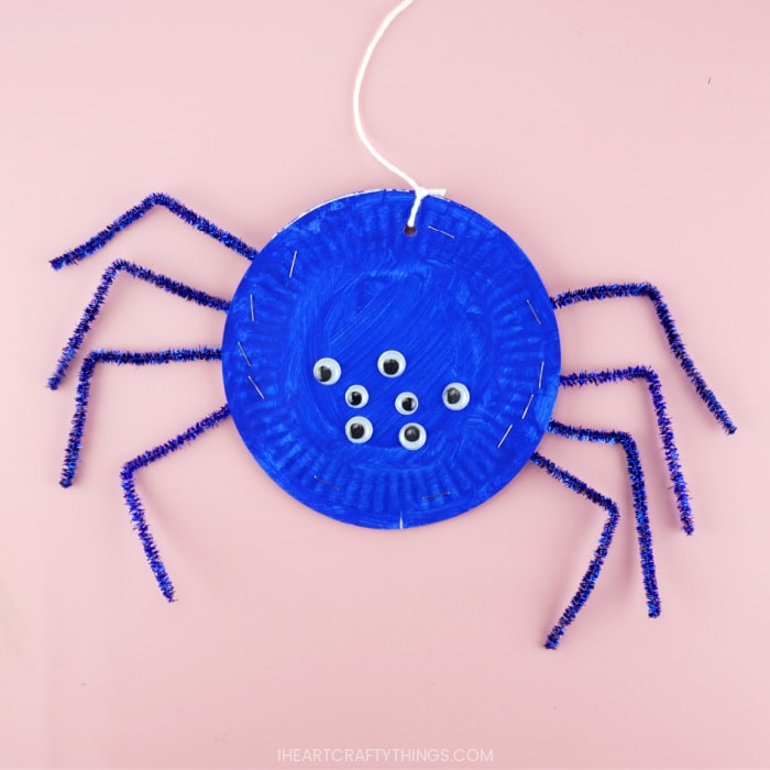 Blue paper plate spider craft laying flat on a pink background.