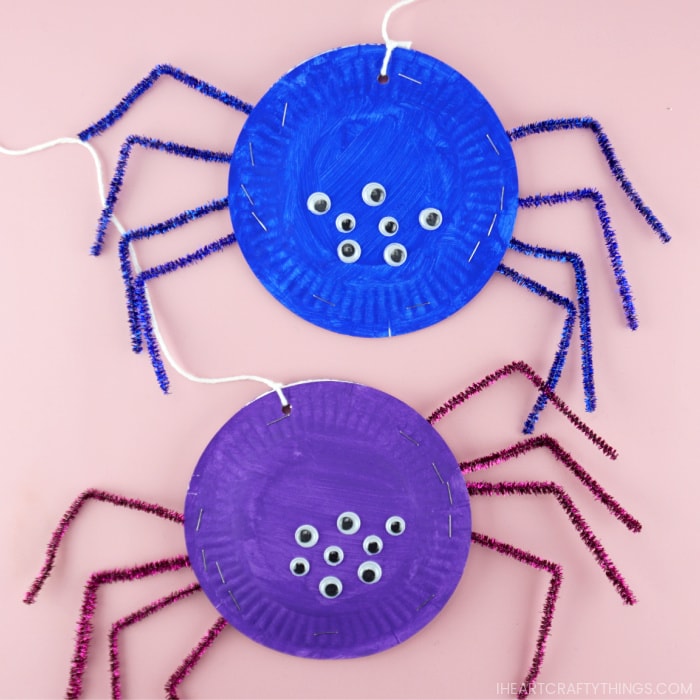 Square image of a purple and blue paper plate spider craft, one on top of the other, laying flat on a pink background.