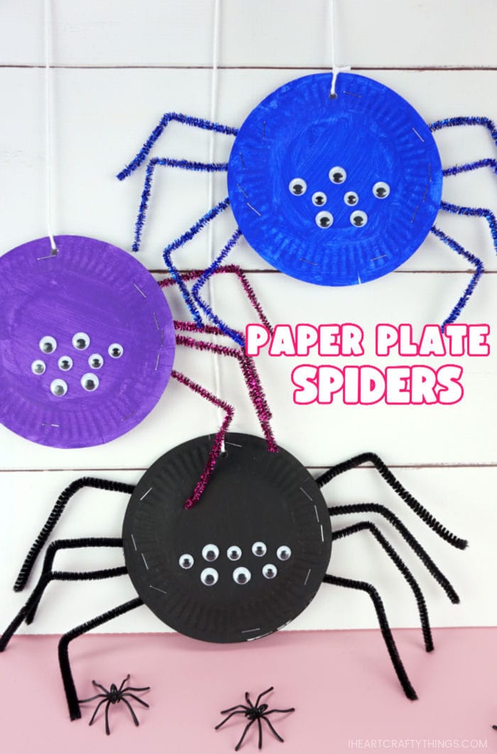 Vertical close up image of three paper plate spiders hanging from a white string on a shiplap background with the words "paper plate spiders" in the right center of the image.