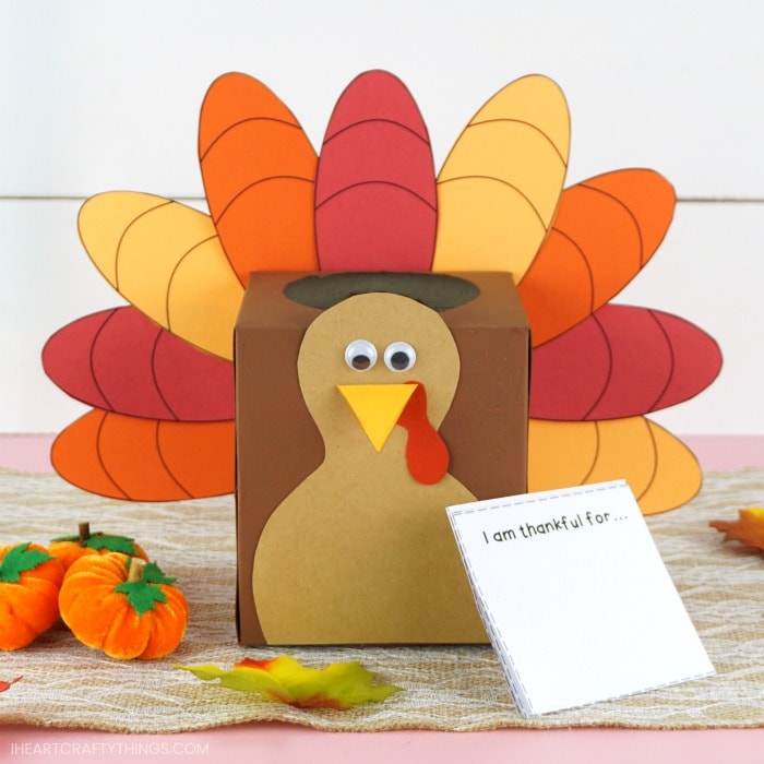 Finished turkey box craft laying on a table with the thankful writing prompt cards propped up on the corner of the box.