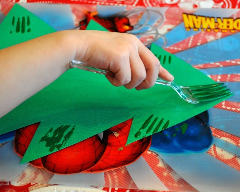 child using a fork to paint the paper Christmas tree