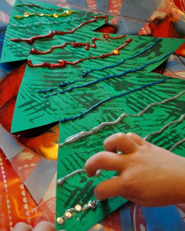 Child decorating their fork painted Christmas tree with glitter glue and sequins.