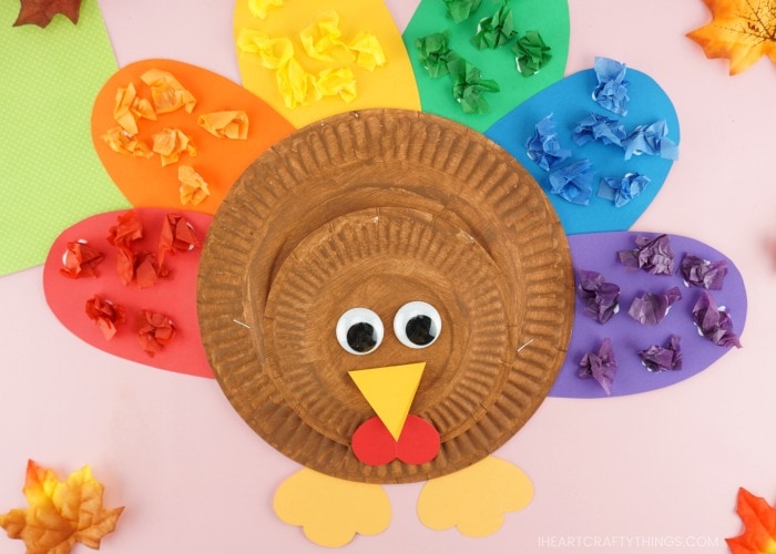 Close up image of completed rainbow paper plate turkey craft laying on a pink background.