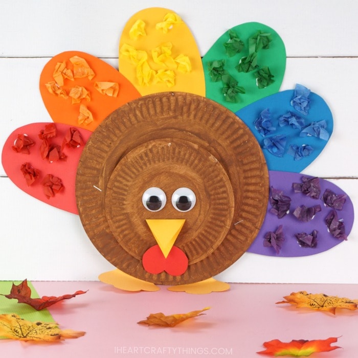 Square image of completed kids turkey craft propped up on a pink table with a white shiplap background and scattered fall leaves laying around it.