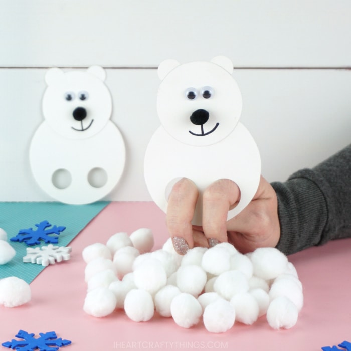 Adult with their fingers inside the polar bear puppet playing with it and using it to knock down a pile of white pom poms.