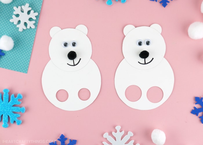 Two polar bear finger puppets laying next to each other on a pink background with snowflake stickers scattered around.