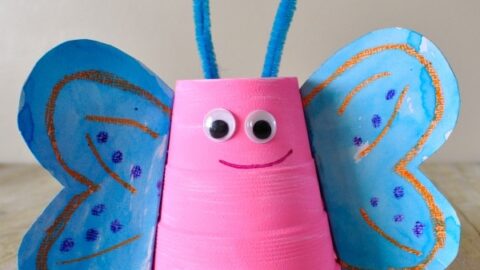 Close up image of pink foam cup butterfly craft with blue wings and blue antennae.