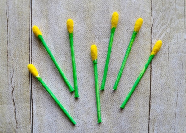 Seven q-tips that have one end cut off and have been painted green with a yellow tip.