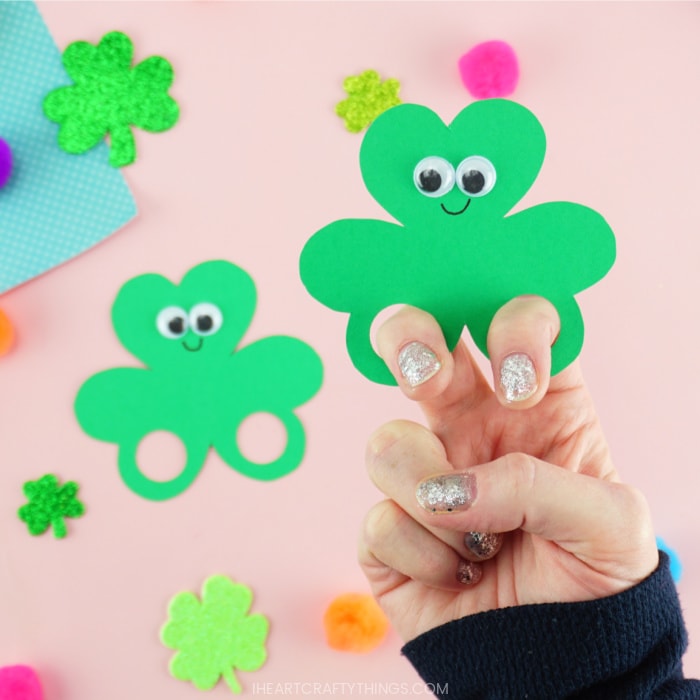 Image of one close up in focus shamrock finger puppet with adults fingers in the holes and one out of focus shamrock puppet laying next to it.