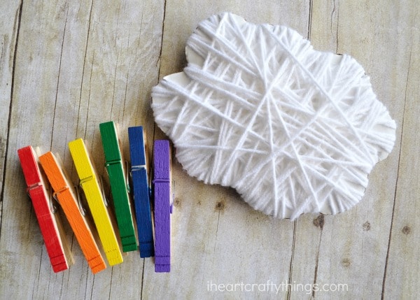 yarn wrapped cloud and painted rainbow clothespins sitting next to each other, ready for a child to assemble together.