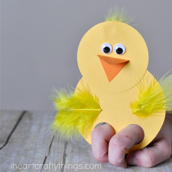 Close up image of child playing with the chick finger puppet made out of paper and yellow feathers.