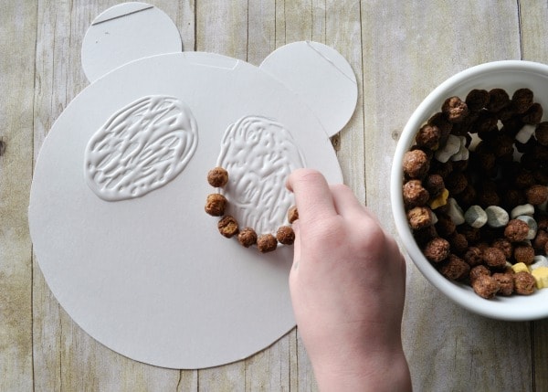 Child gluing cereal on the cardboard panda shape.