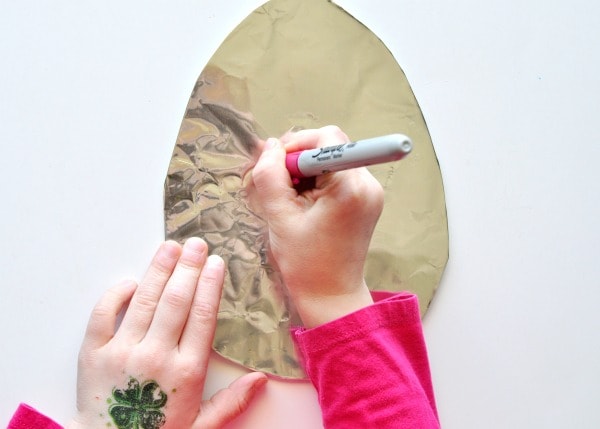 Child using a sharpie to decorate a tin foil covered cardboard Easter Egg shape.