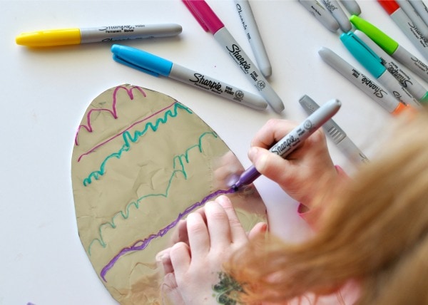 Child using a purple Sharpie marker to decorate a tin foil covered cardboard Easter Egg shape.