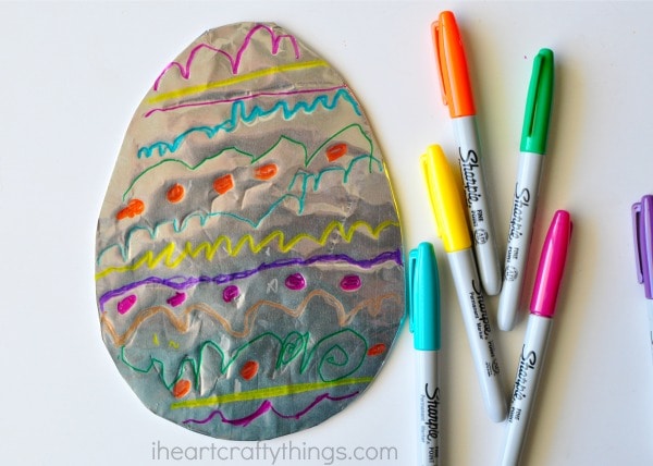 Blue, yellow, orange, green and pink Sharpie markers laying next to a decorated tin foil Easter Egg.