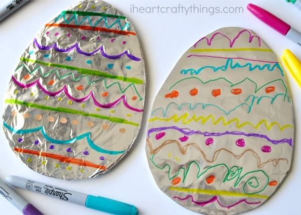 Side angle of two decorated tin foil Easter eggs laying next to each other.