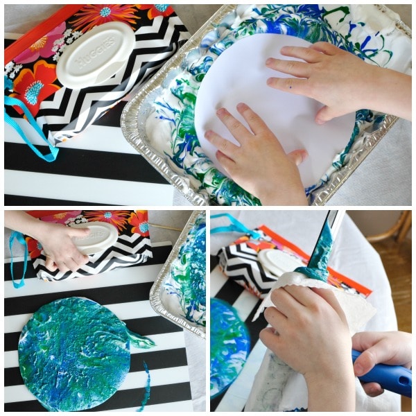 child dipping a white paper circle into marbled paint and removing the paint from it to show the marbled effect