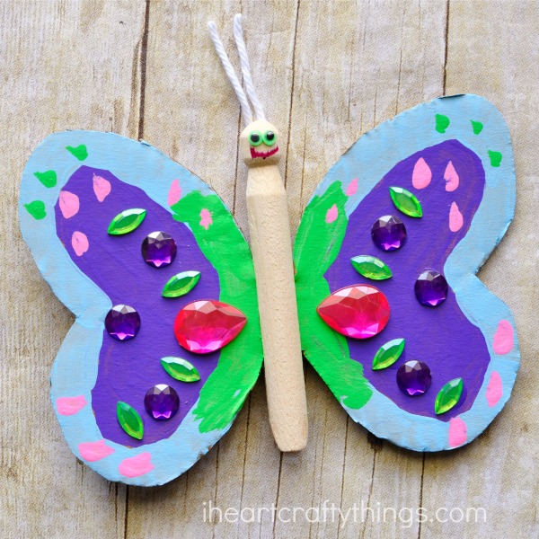 wooden peg and cardboard butterfly craft laying on a faux wood background