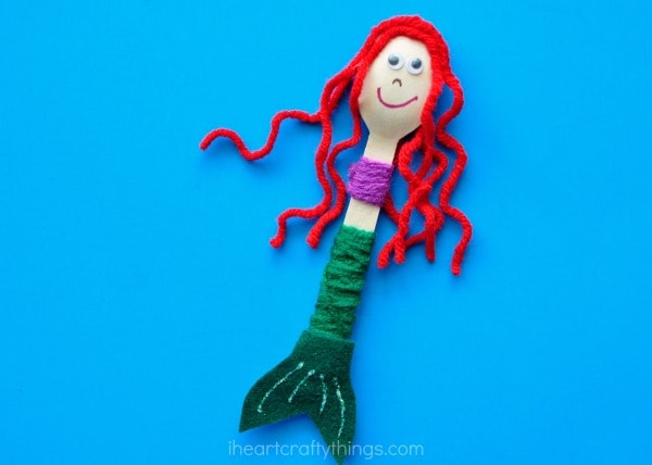 red-headed wooden spoon mermaid laying flat on a blue background