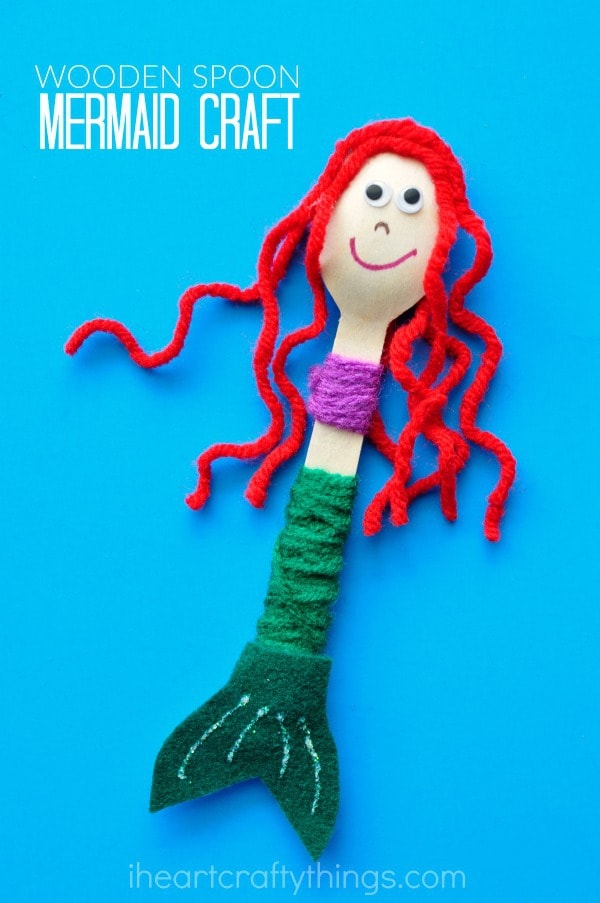 close up vertical image of red-haired wooden spoon mermaid craft laying on blue background