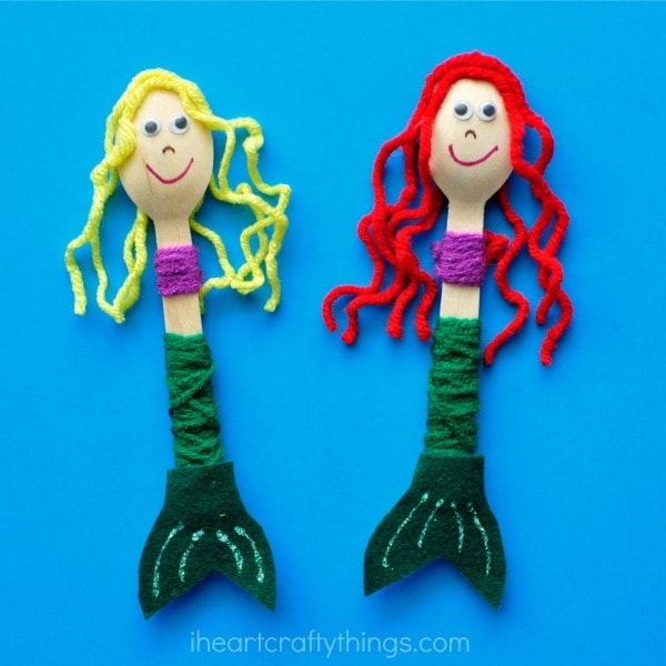 blonde haired and red haired wood spoon mermaid dolls laying flat on blue background