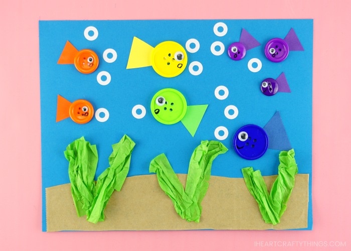 horizontal image of completed button fish craft project laying on a pink background