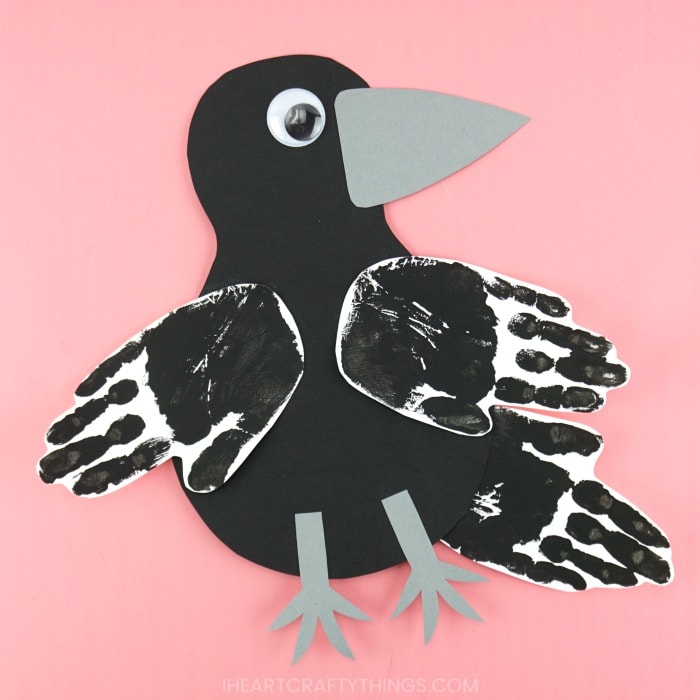 Finished handprint raven craft laying flat on a pink background.