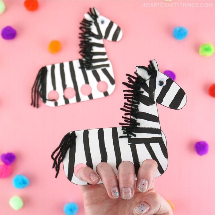 Close up image of person with their fingers inside the zebra finger puppet with another finger puppet out of focus in the background.