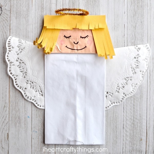 Paper bag angel craft laying on a white wood background.