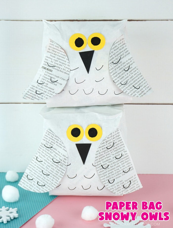 Vertical close up image of two snowy owl crafts one laying on top of the other in front of a white shiplap background with the text "paper bag snowy owls" in the bottom right corner.