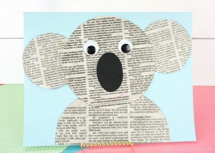 horizontal image of newspaper koala craft propped up pink table with white shiplap background