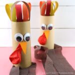 Finished examples of turkey windsock crafts standing straight up with white shiplap background.