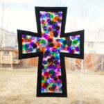 Square photo of a stained glass cross craft hanging in a window