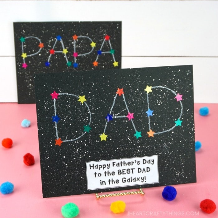 Father's Day DAD constellation craft placed on a photo stand on a pink table with colored craft poms and a blurry white shiplap background