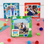 Square image of three Father's Day photo frame crafts. Front craft is in focus and back two are out of focus in front of a white shiplap background