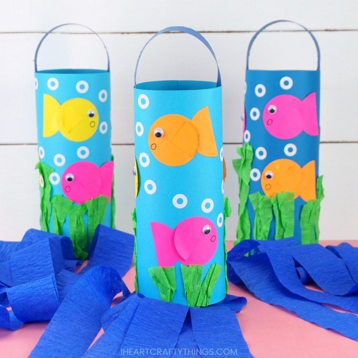 Square image of three DIY fish windsocks on a pink table with white shiplap background. Middle windsock is in focus and two back windsocks are blurry.