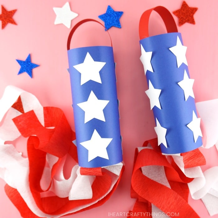 Two red, white and blue patriotic windsocks laying flat on a pink background with glitter star stickers scattered around.