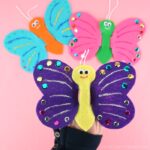 Close up image of someone playing with the butterfly finger puppet with two more puppets out of focus in the backrground.
